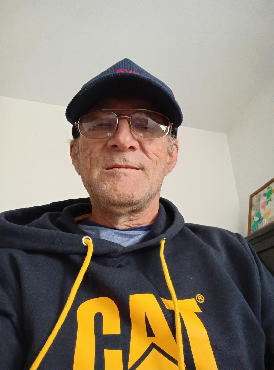 A man wearing a blue cap, glasses, and a dark blue hoodie with a yellow 'CAT' logo.