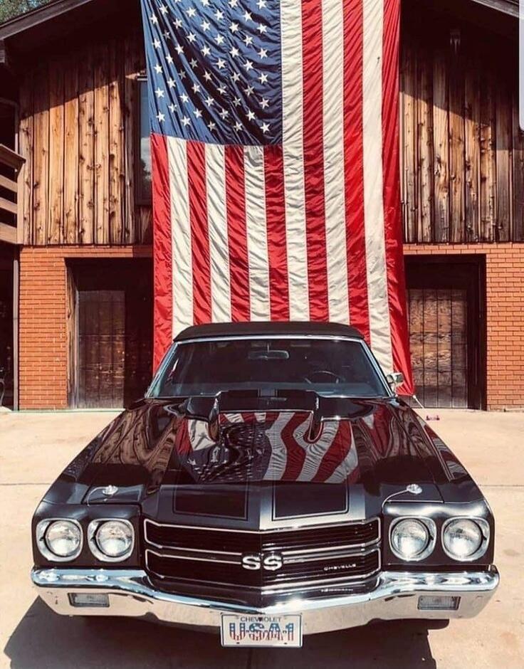 USA (license plate) and SS (grille emblem) on a classic Chevrolet car in front of a large American flag.