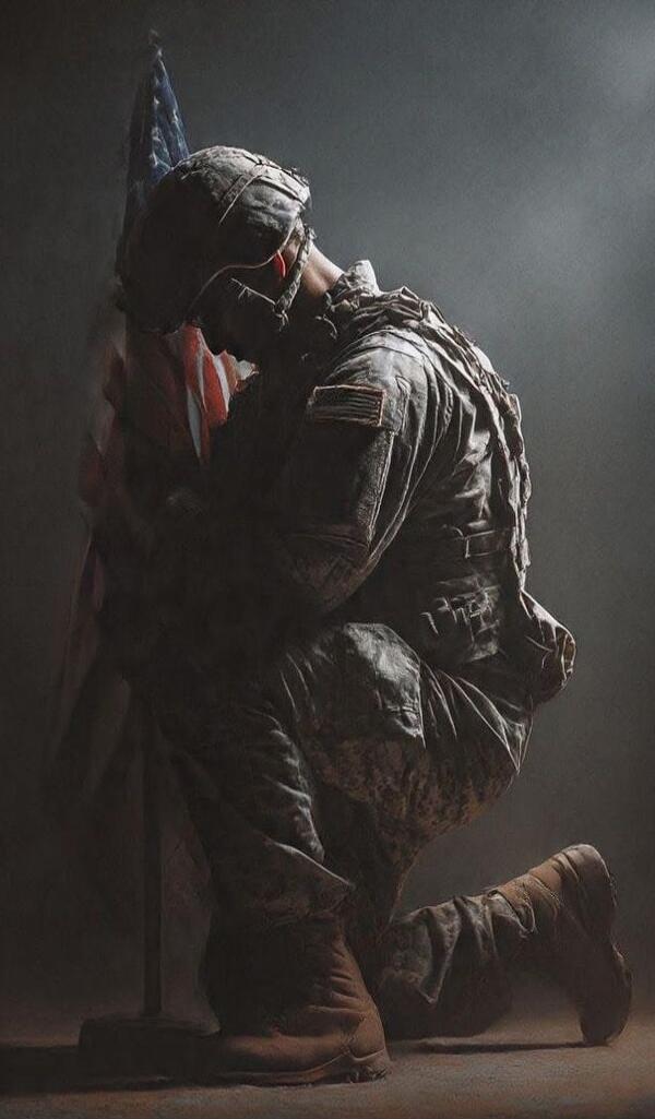 A kneeling soldier praying beside an American flag.