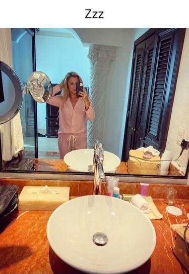 Zzz. A woman in pink pajamas takes a selfie in a bathroom mirror.