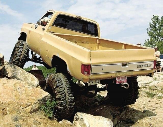 Yellow old pickup truck off-roading on rocky terrain with large tires.