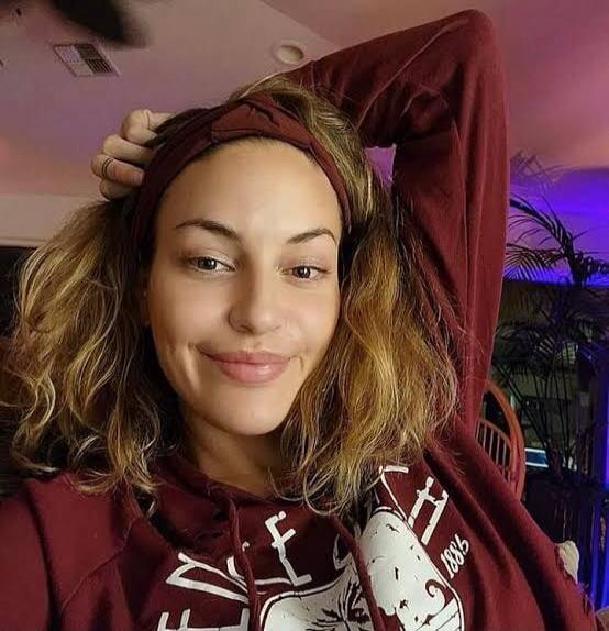 A woman smiling at the camera, wearing a maroon hoodie and a headband.