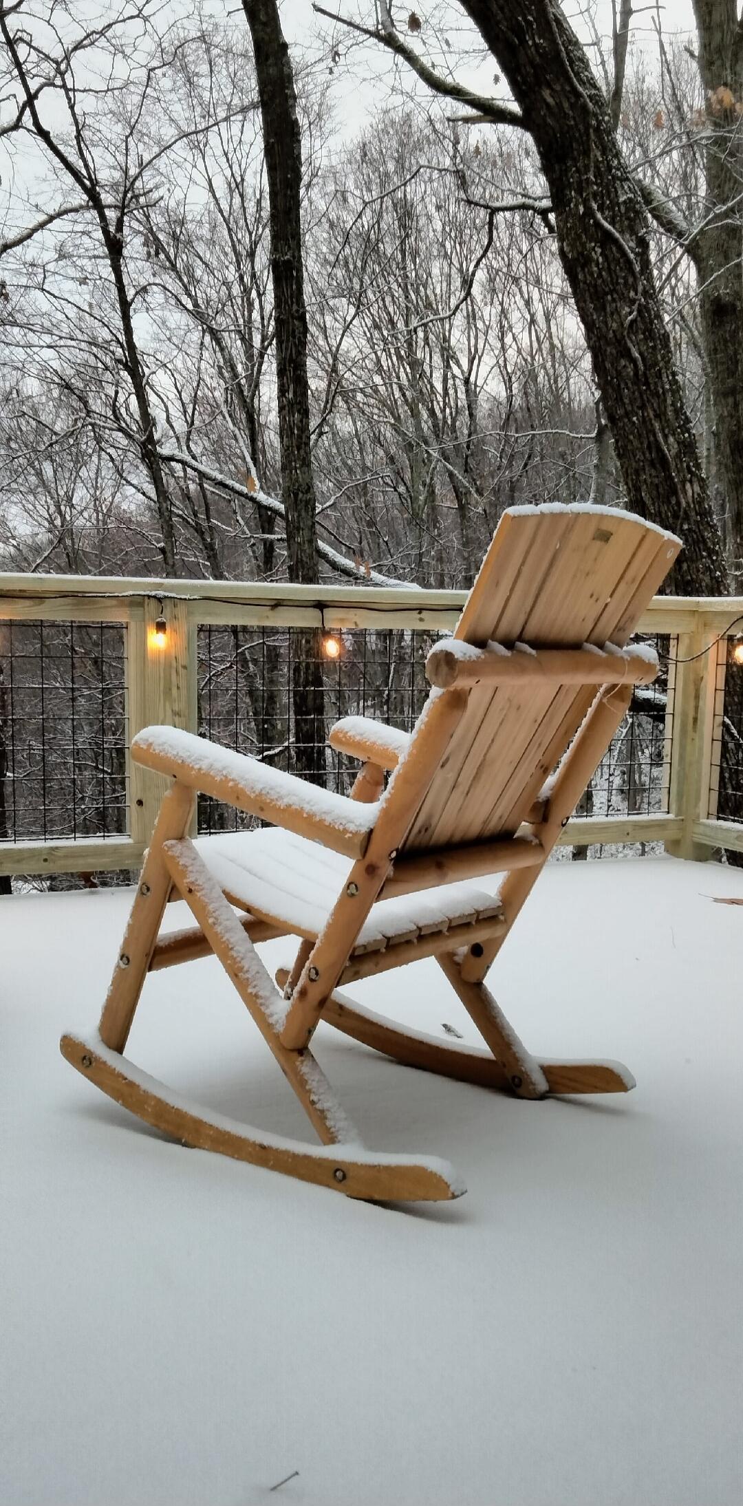 A wooden rocking chair on a snow-covered deck.