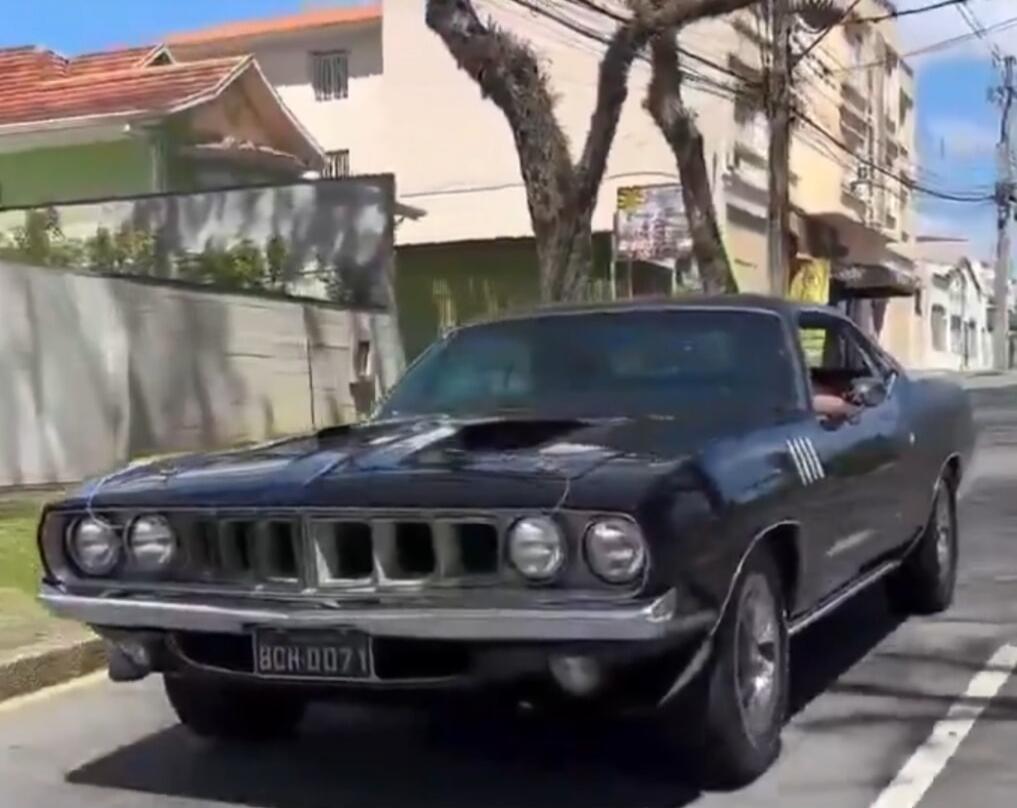 A vintage dark-colored classic car is driving on a city street.