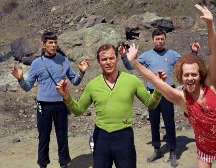 Three Star Trek characters (Spock, Captain Kirk, and Dr. McCoy) in their uniforms are standing in a rocky outdoor setting with their hands raised. Next to them, Richard Simmons, in a sparkly red leotard, is enthusiastically posing with his arms up and a wide smile.