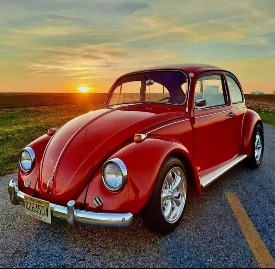 A red vintage Volkswagen Beetle parked on a road at sunset.