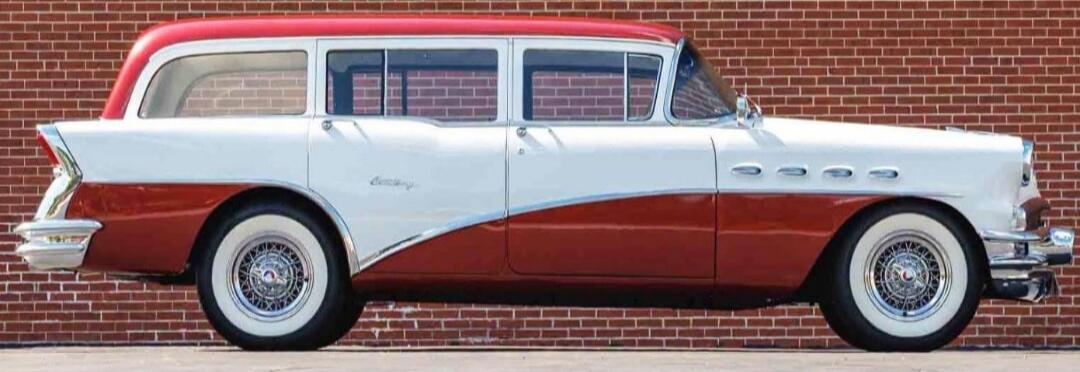 A classic two-tone red and white station wagon car is parked in front of a brick wall.