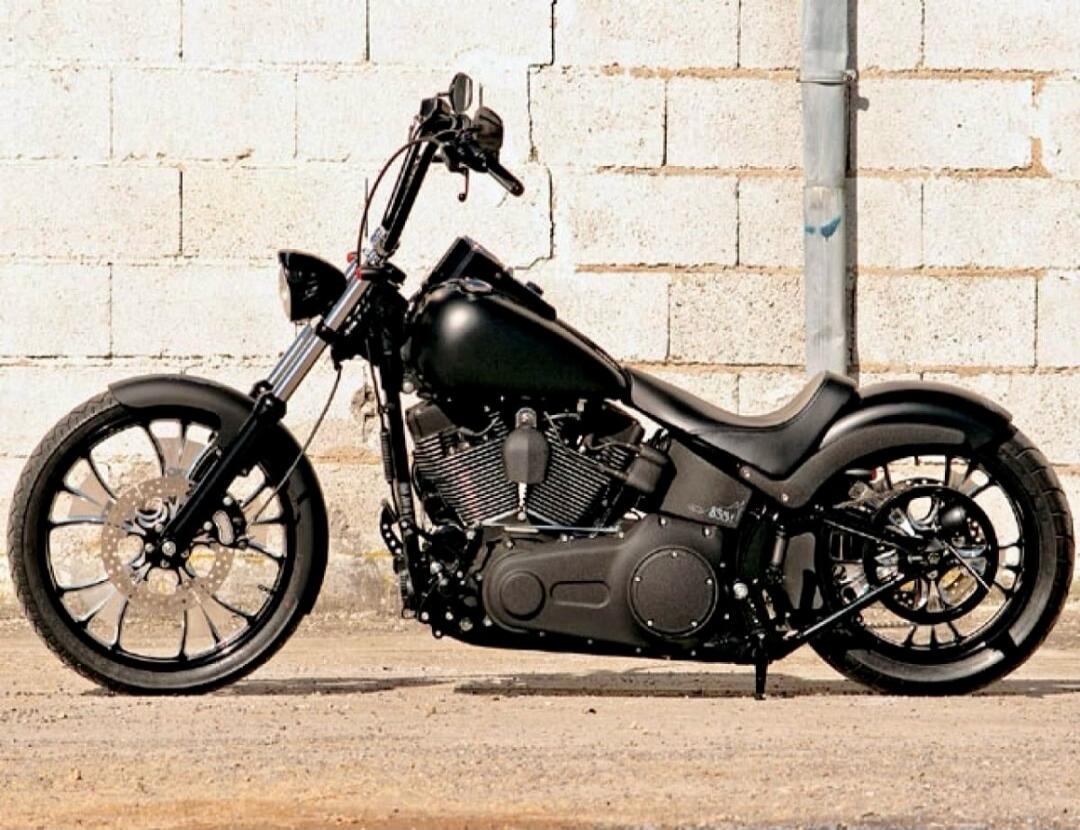 A custom black motorcycle is parked against a white brick wall.