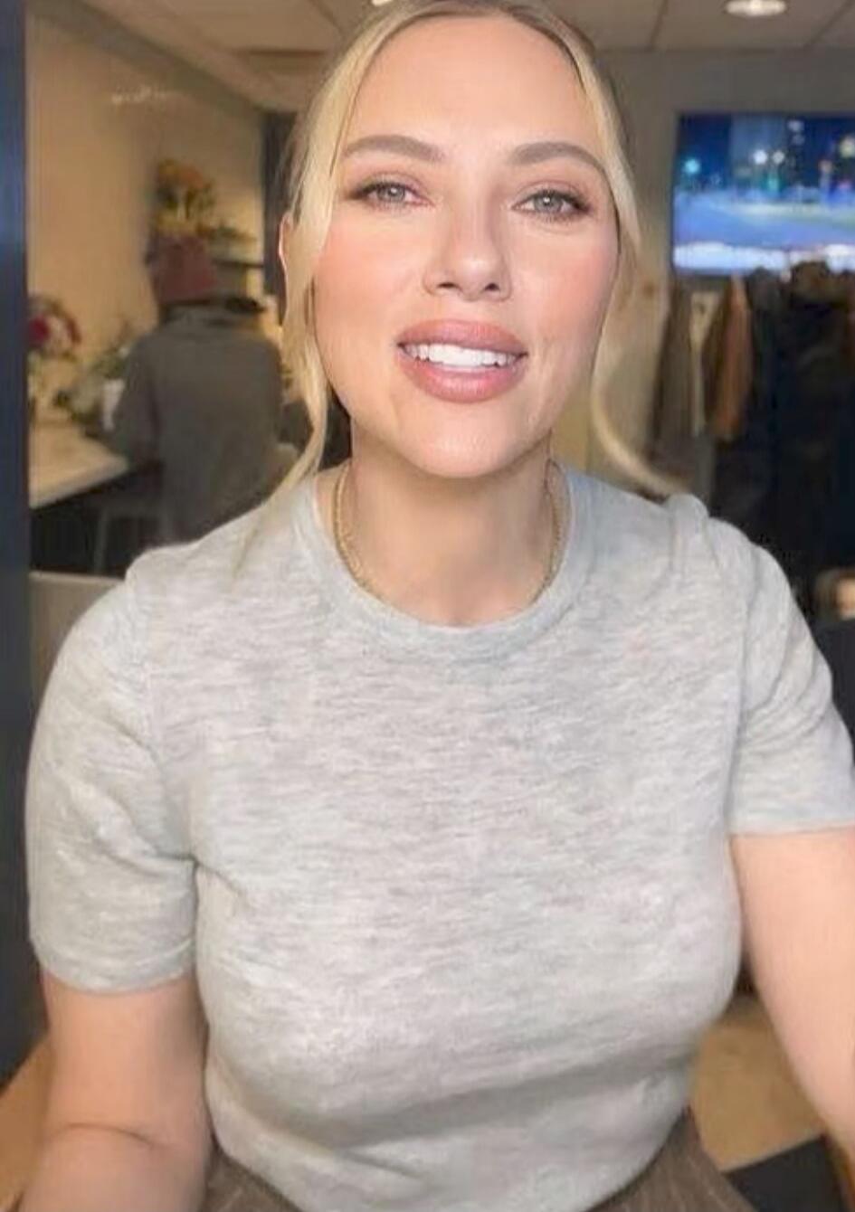 A woman with blonde hair wearing a gray t-shirt smiling at the camera in an indoor setting.