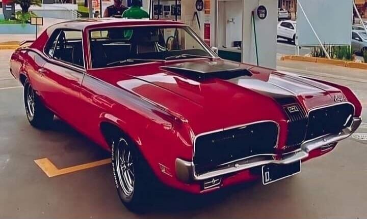 Red classic car with black hood scoop parked in a lot