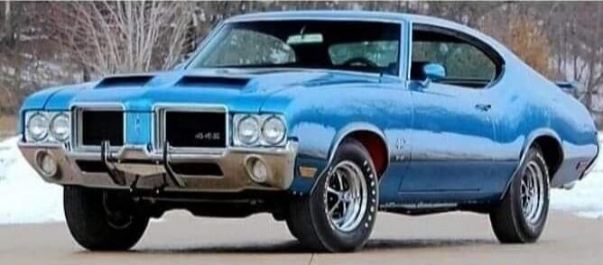 A classic blue Oldsmobile 442 muscle car is parked outdoors with a snowy background.