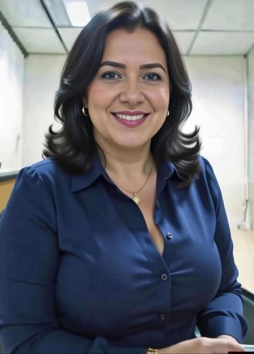 Portrait photo of a smiling woman wearing a navy blue blouse and gold jewelry, indoors.
