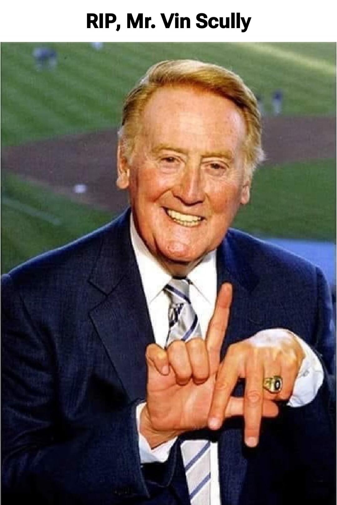 RIP, Mr. Vin Scully. A man in a suit smiles and makes an 'LA' hand gesture, likely referring to Los Angeles, with a baseball field in the background.