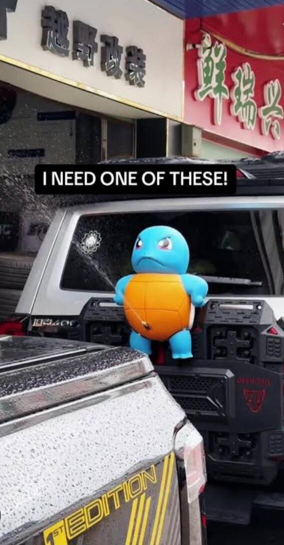 I NEED ONE OF THESE! A Squirtle figure is attached to the back of a car, spraying water from its mouth, seemingly acting as a fun car wash accessory or a decorative water feature.