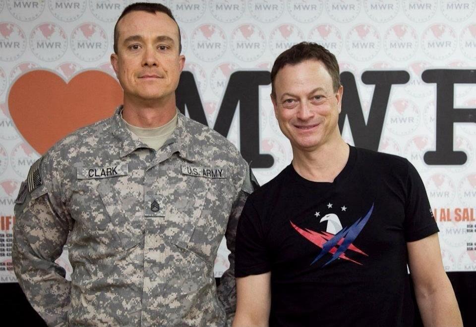 Two men are posing for a photo. The man on the left is wearing a U.S. Army uniform with the name tag 