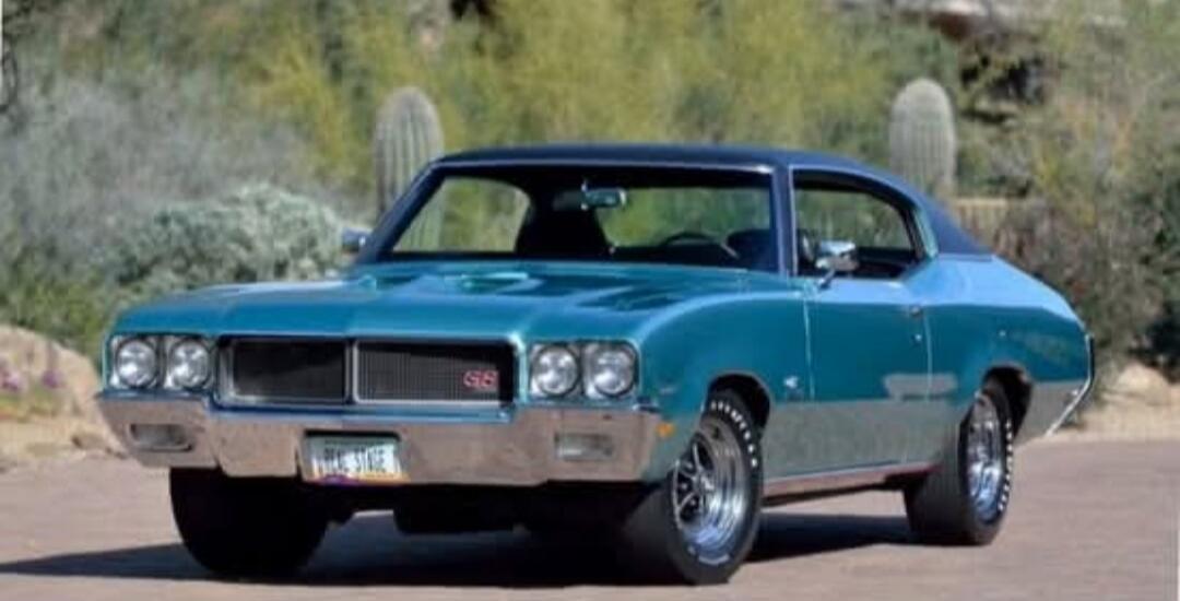 Blue vintage muscle car (front/three-quarter view) in a desert setting.