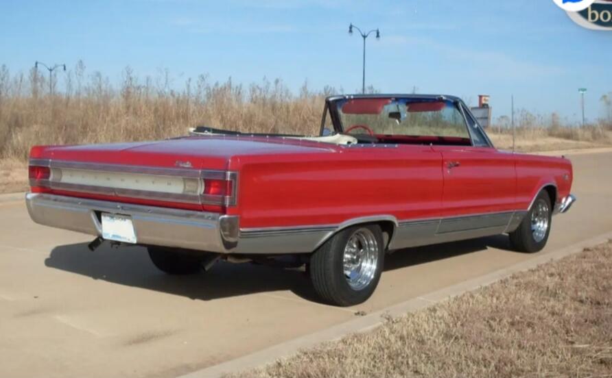 A red vintage convertible car parked on a sunny road, with its top down and classic chrome details. Dry grass and clear blue sky in the background.