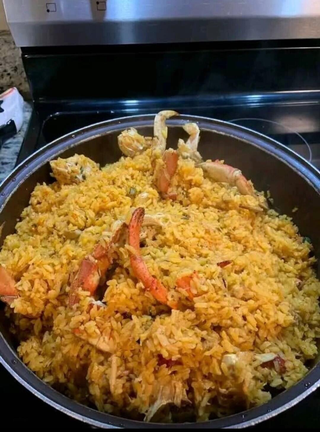 Large pot of yellow fried rice with assorted seafood pieces (shrimp/crab) mixed in.
