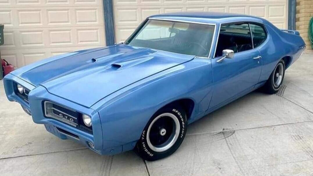Blue classic car parked in a driveway in front of a garage.