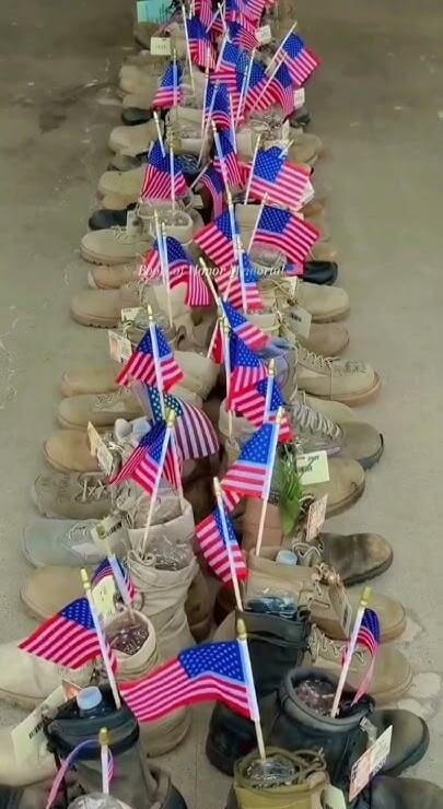 In Honor Memorial. A solemn display of numerous military boots, each adorned with a small American flag, arranged in rows as a tribute.