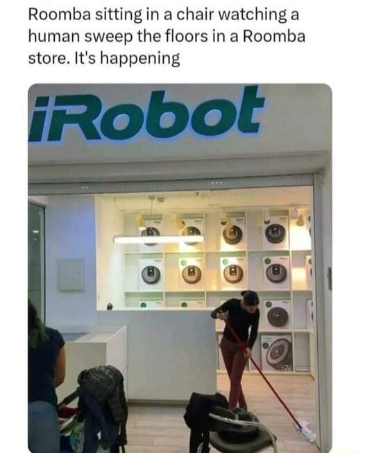 Roomba sitting in a chair watching a human sweep the floors in a Roomba store Its happening