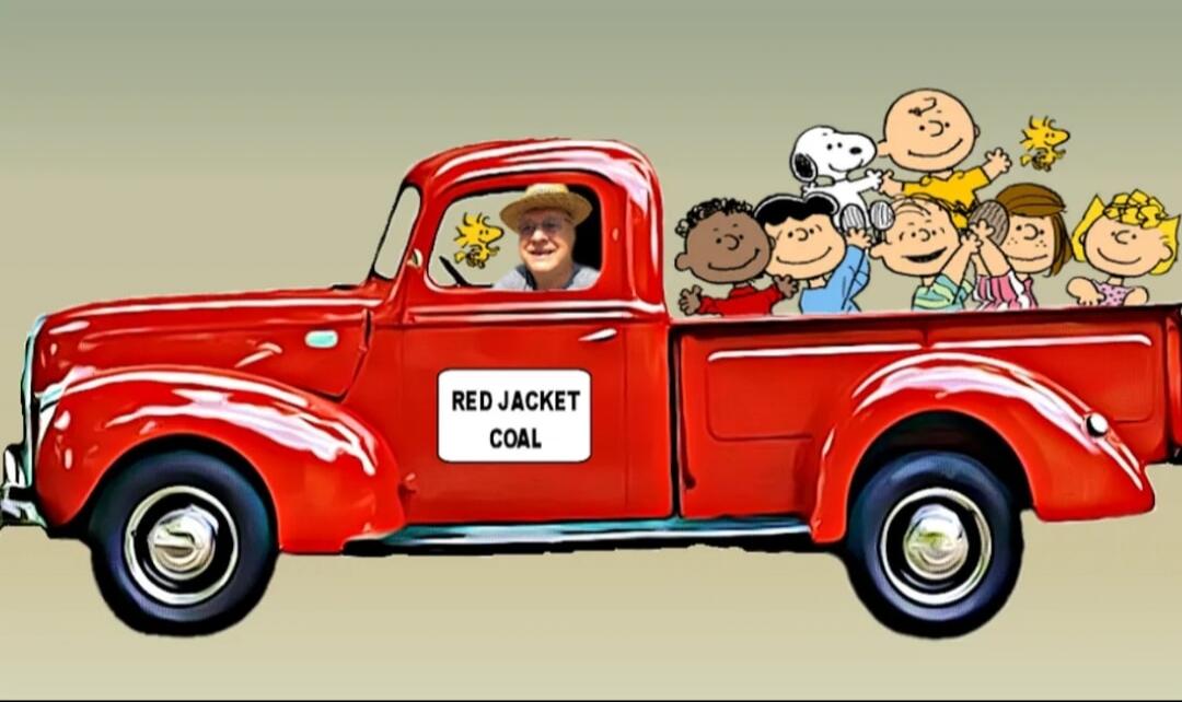 A man in a straw hat is driving a red vintage pickup truck. In the back of the truck, several Peanuts characters including Snoopy, Woodstock, Charlie Brown, and others are riding. The truck has 'RED JACKET COAL' written on its side.