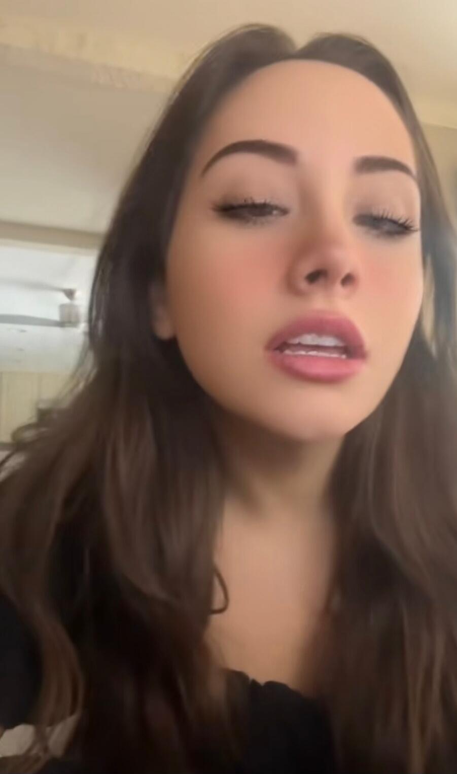 Close-up selfie of a young woman with long brown hair, eyes half-closed, mouth slightly open.