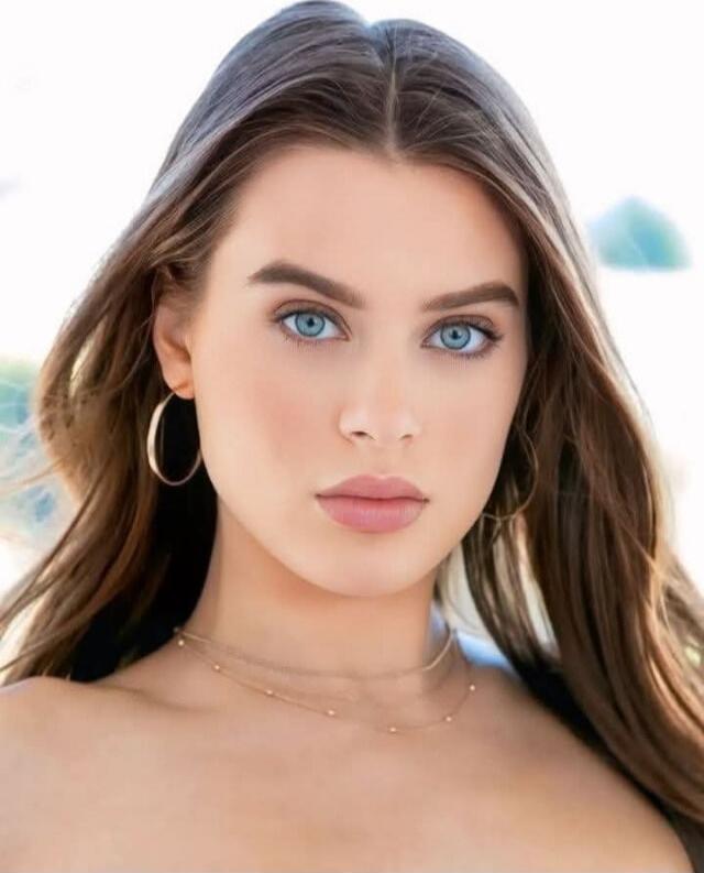 Portrait of a young woman with blue eyes, hoop earrings, and subtle makeup.