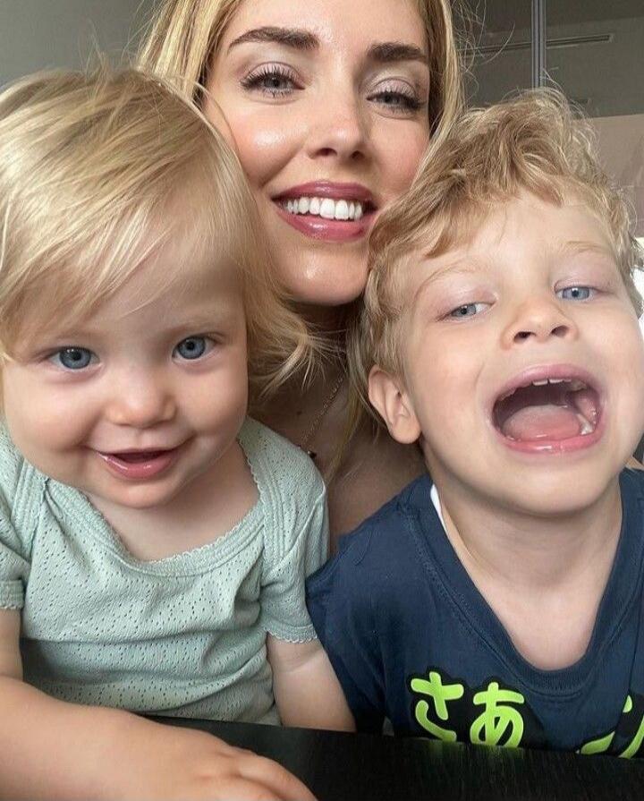 A woman taking a selfie with two young children, all smiling at the camera.