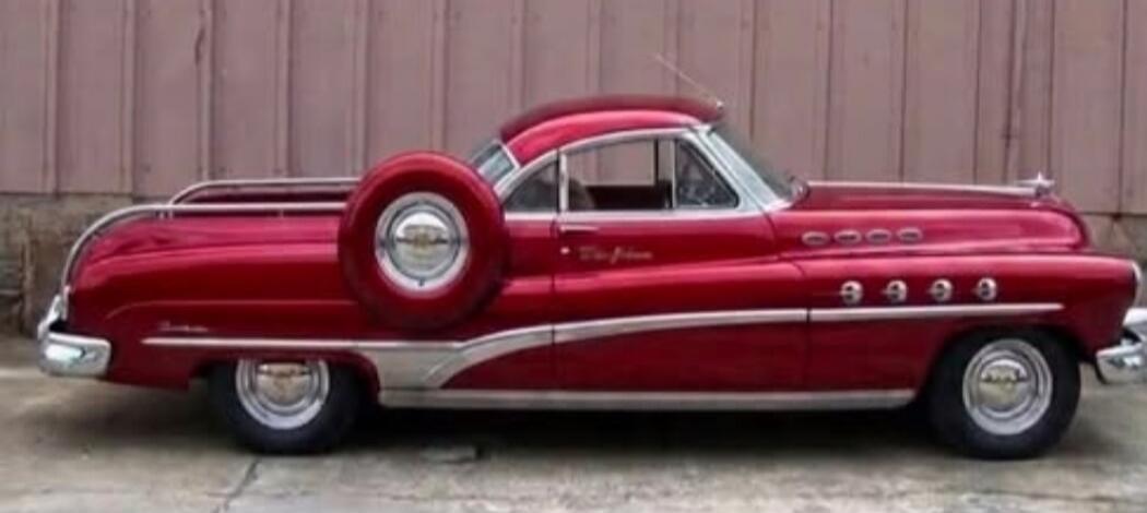 A classic red car with a spare tire mounted on the side, featuring chrome accents and a sleek design, parked against a plain background.