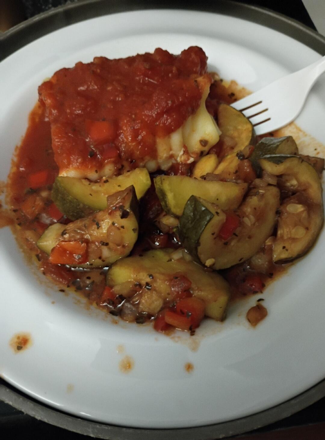 A plate with a tomato-sauce covered dish and sautéed vegetables (zucchini, eggplant, peppers) on a white plate.