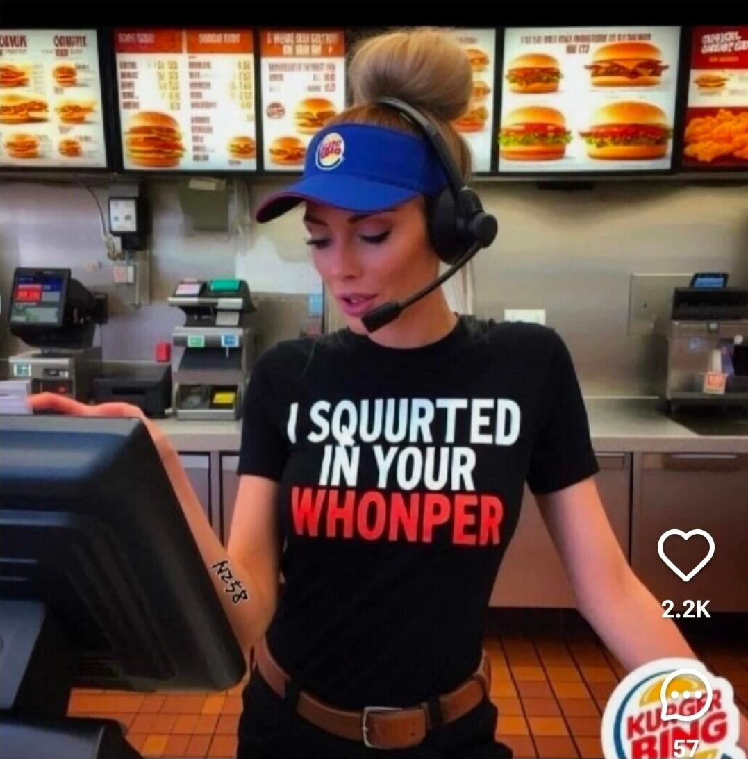 A woman wearing a Burger King visor and headset is standing at a counter. She is wearing a black t-shirt with the text 'I SQUURTED IN YOUR WHONPER'. Menu boards with various burgers are visible in the background. A '2.2K' likes counter and a partially visible, distorted Burger King logo are also present.