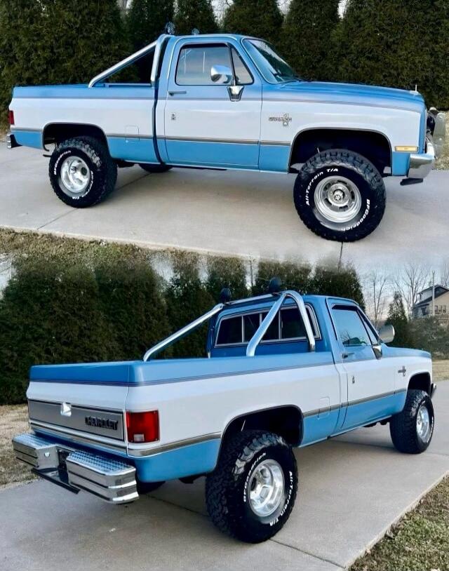 Two-tone blue and white vintage pickup truck with lifted tires, roll bar, and chrome bumper.