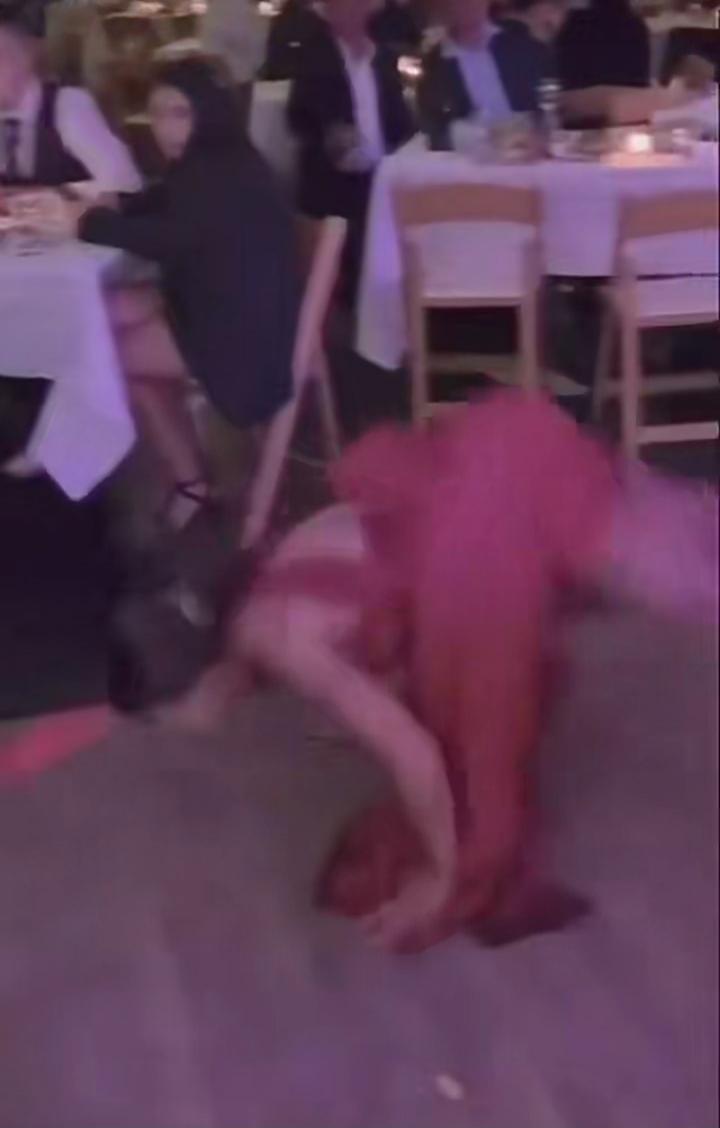 A person on the floor performing a dance move at a formal event; others seated at tables watching.
