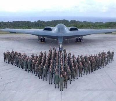 A large group of soldiers standing in formation in front of a stealth bomber on a runway.