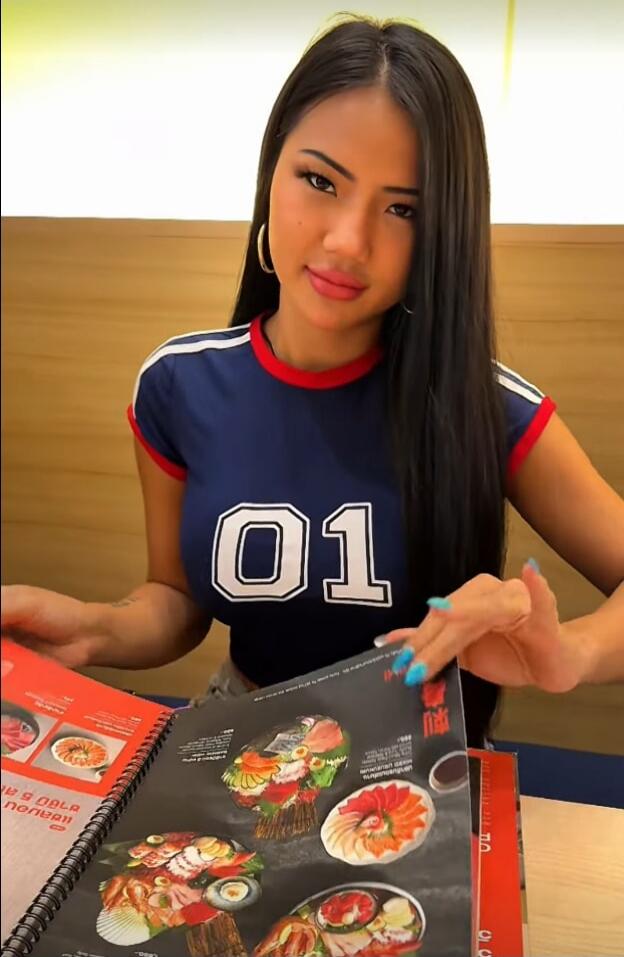 A woman wearing a blue crop top with '01' printed on it is looking at a menu with various food items.