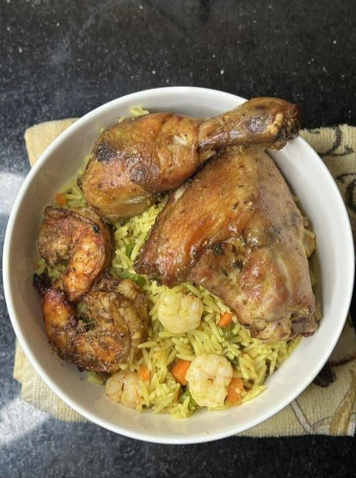 A bowl of yellow rice with roasted chicken pieces (drumstick and thigh) and vegetables.