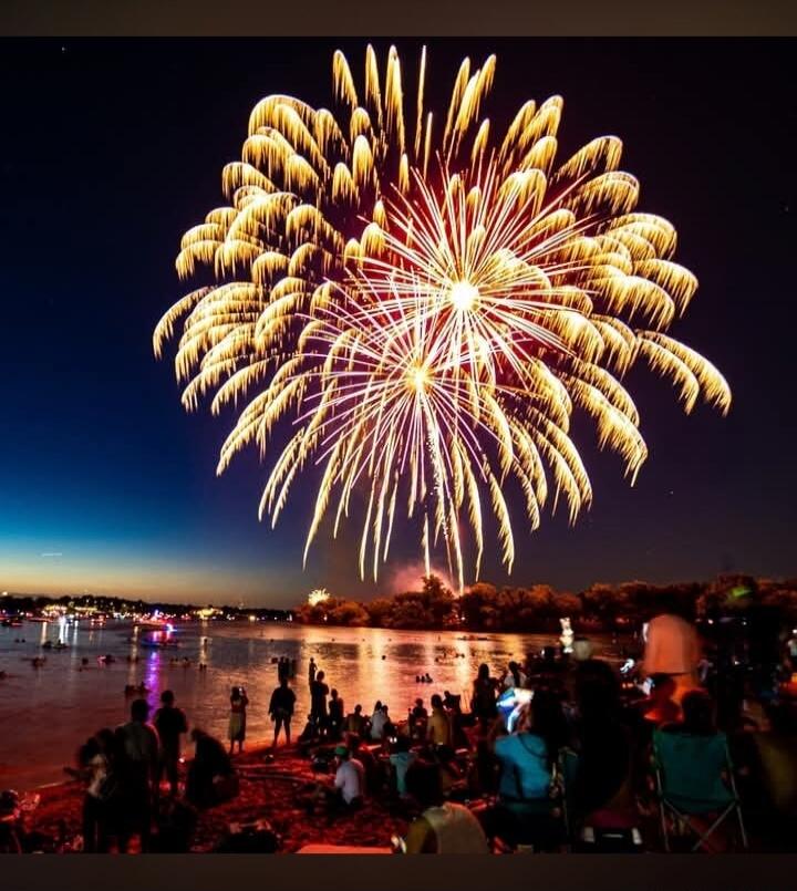 Beautiful fireworks over the lake at night with people watching from the shore