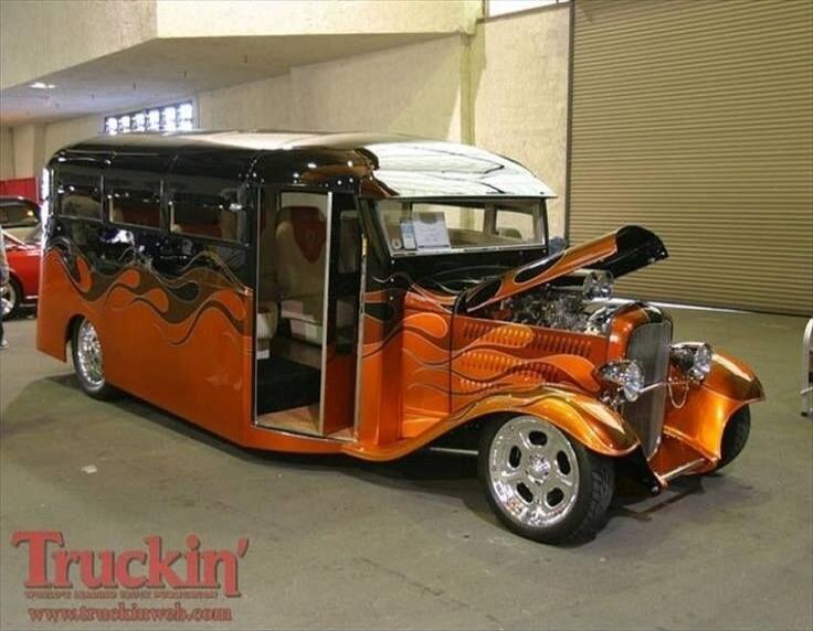Truckin' www.truckinweb.com. A highly customized orange and black hot rod bus with flame decals and an open engine hood, displayed at a car show.