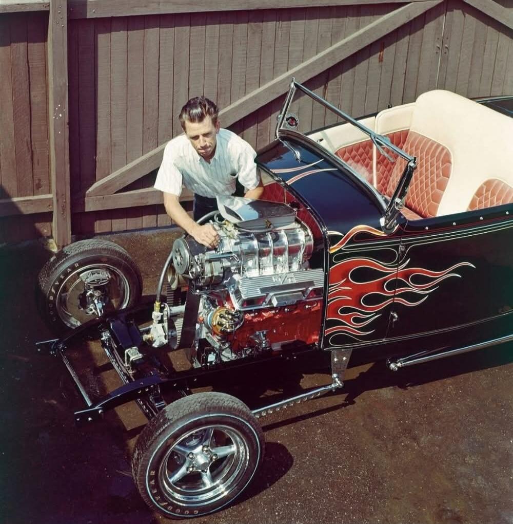 A man is working on the engine of a hot rod car.