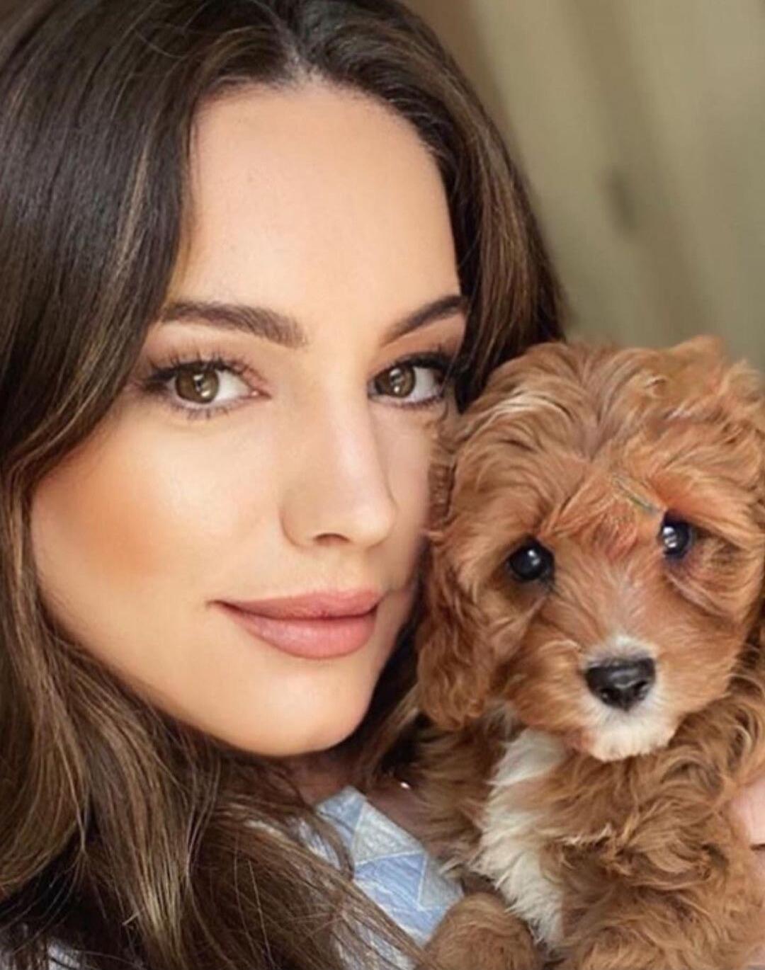 A woman posing with a small brown fluffy puppy.
