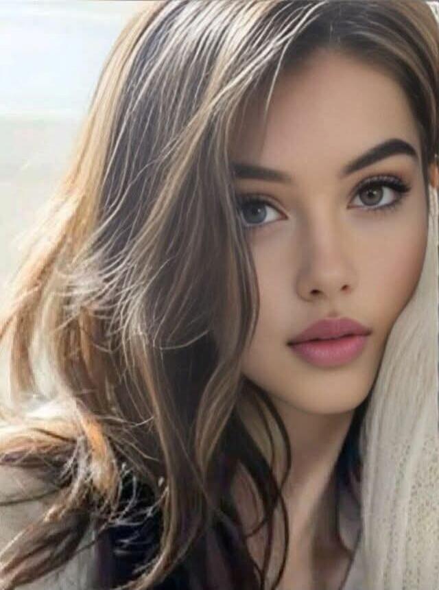 A close-up portrait of a young woman with long wavy hair, subtle makeup, pink lips, and a soft expression.