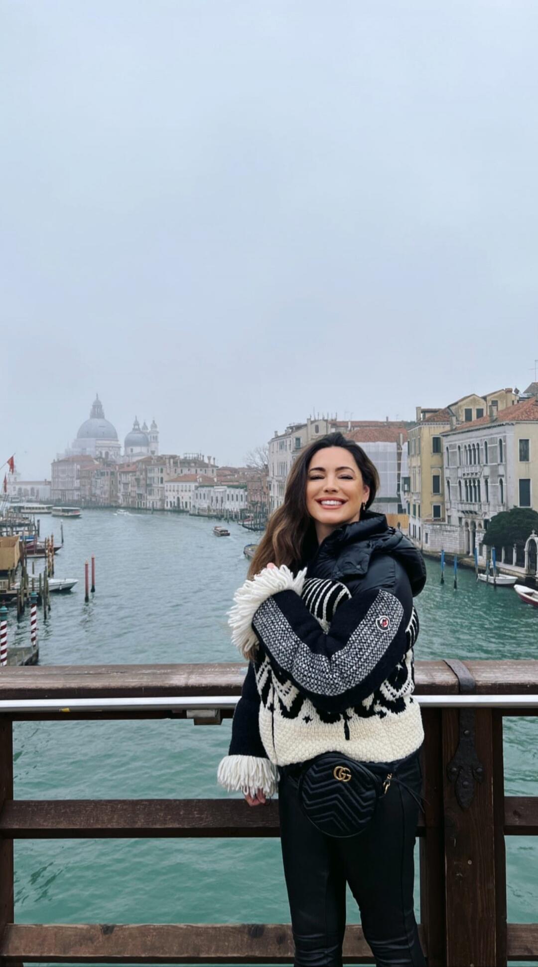 Woman standing on a wooden bridge by a canal in Venice, Italy, smiling.