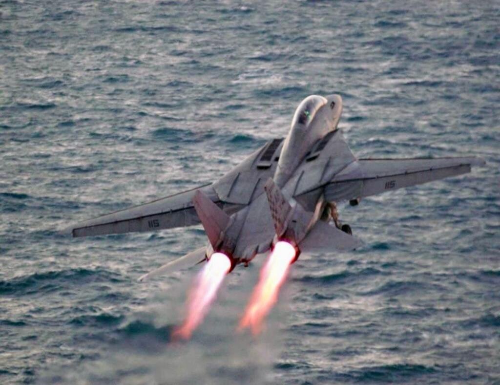 military fighter jet taking off from the ocean with afterburners