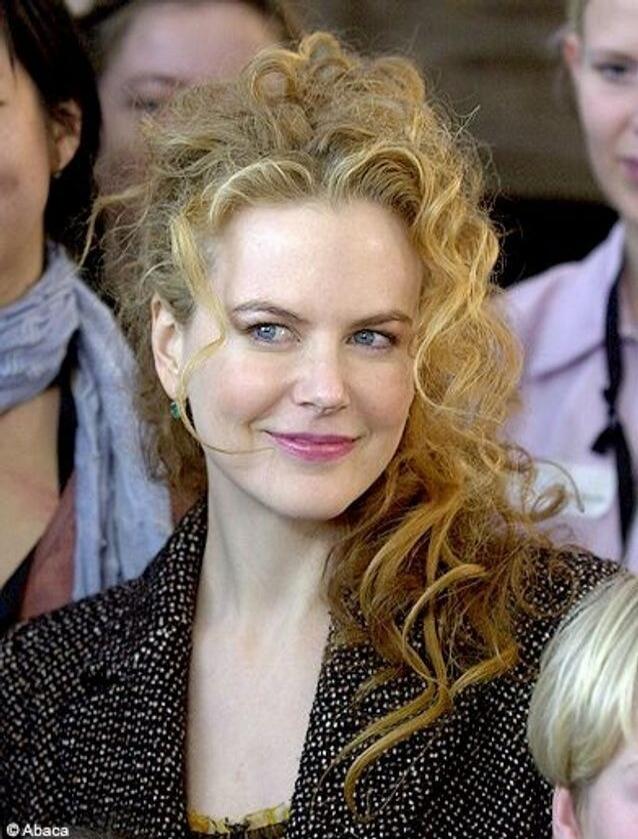 A portrait-style photo of a smiling woman with curly red hair, wearing a dark speckled coat.