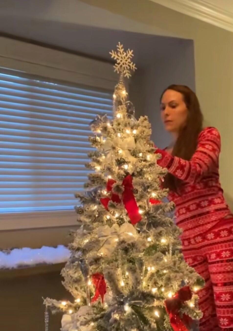 A woman decorating a white Christmas tree with lights indoors.