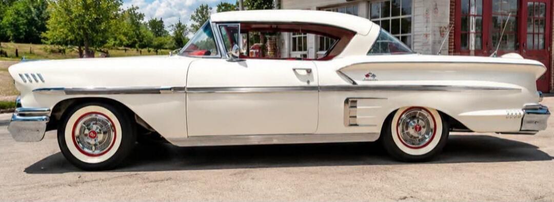 A classic white car with a red interior and whitewall tires, parked outdoors.