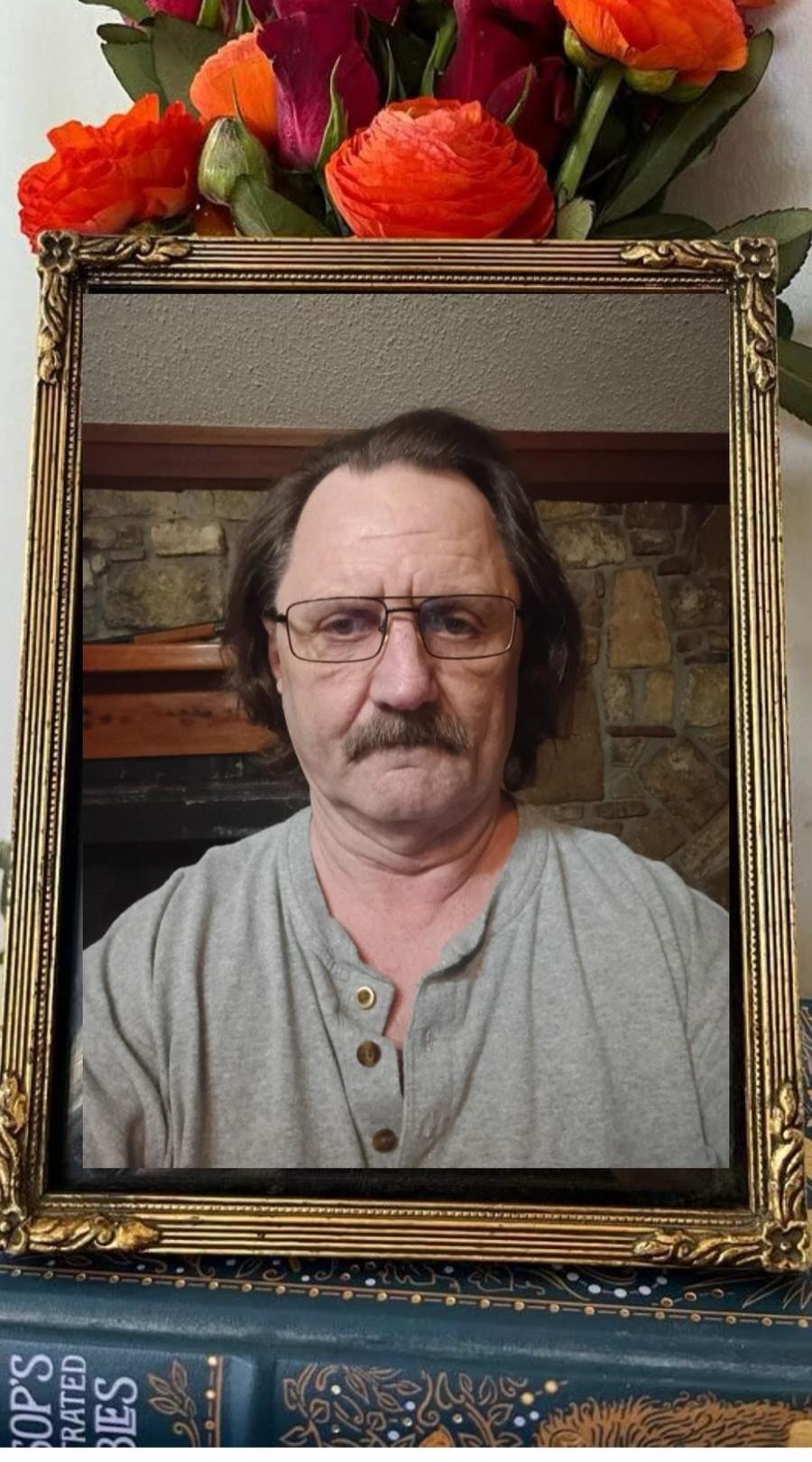 Portrait of a man with glasses and mustache inside a decorative frame, with bright orange flowers above the frame.