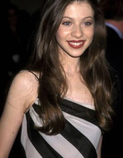A portrait of a young woman with long brown hair wearing a black-and-white striped dress at what appears to be a formal event.