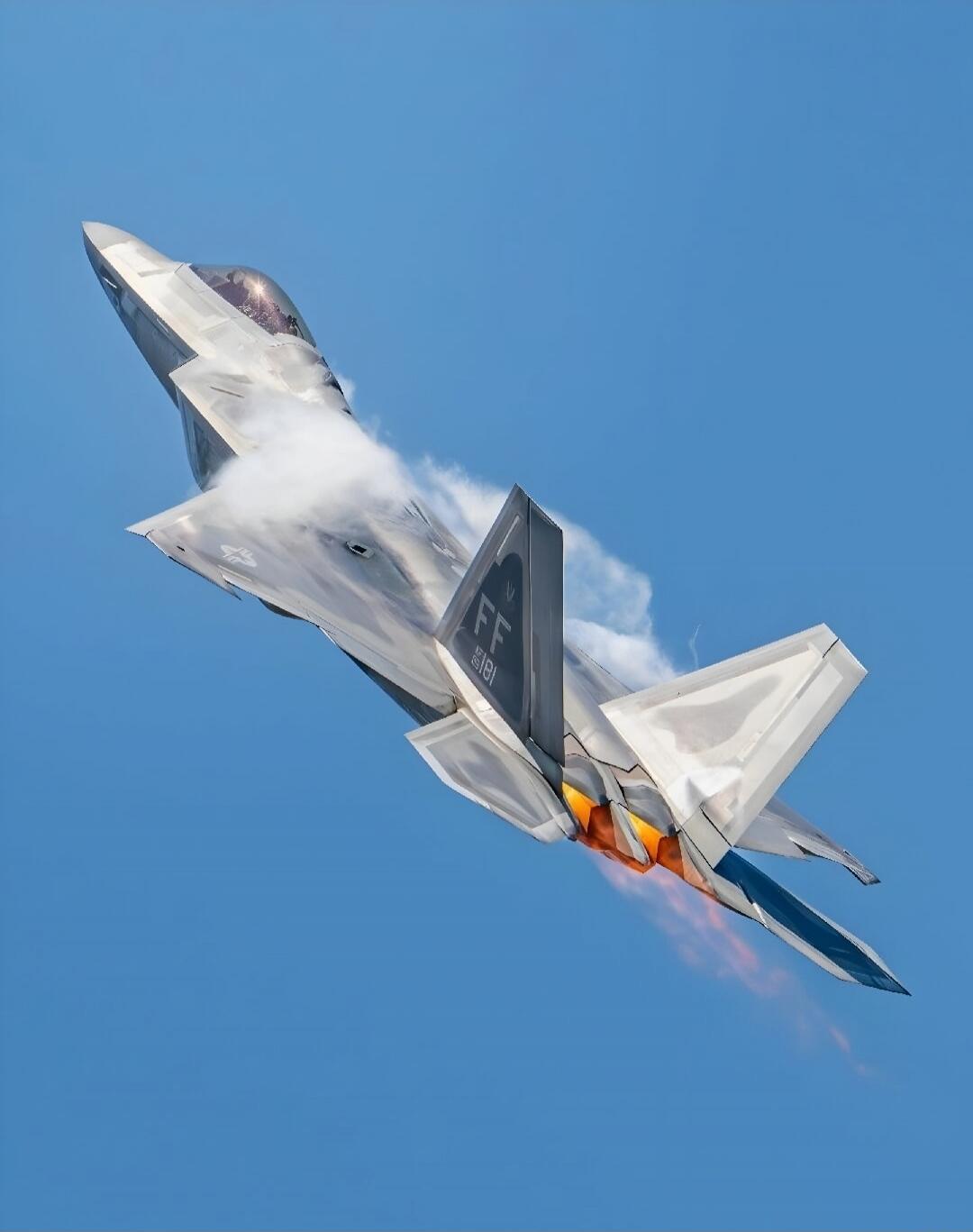 A military fighter jet performing a high-speed aerobatic maneuver with afterburners visible against a clear blue sky.